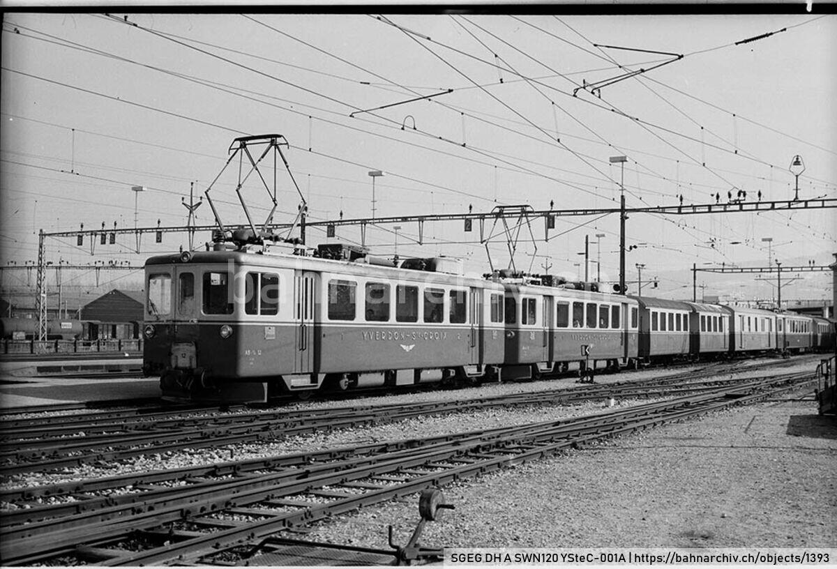 SGEG DH A SWN120 YSteC-001A: Zug der Compagnie du Chemin de fer d'Yverdon à Sainte-Croix (YSteC) mit Triebwagen ABe 2/4 12 und ABe 2/4 11 sowie Personen- und Gepäck/Postwagen in Yverdon